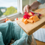 Man scraping food from his cutting board into the trash (food waste)