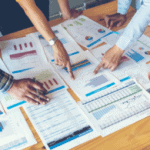 team of hands pointing at different papers while analyzing sales