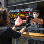 restaurant employee handing a to-go order over to a customer outside wearing masks