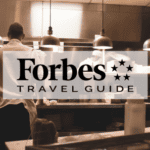 Forbes Travel Guide logo in front of a kitchen at a restaurant.